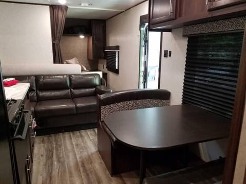 Inside view of Camper B featuring dinette table, sleeper sofa, queen bed in back and kitchen.