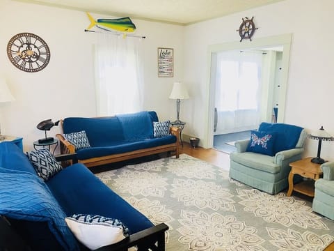 Cozy living room has fan, two chairs, two queen-sized futons, & smart tv.