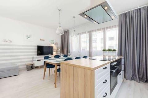 The open-plan kitchen features white cabinets, a wooden countertop, and modern appliances, seamlessly connected to a dining area with a sleek table and blue chairs.