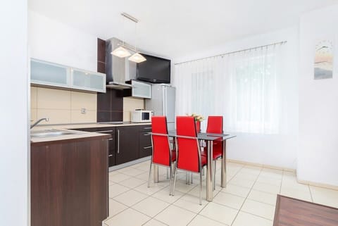 The dining area features a table with red chairs. The kitchen is equipped with dark cabinets and stainless steel appliances.