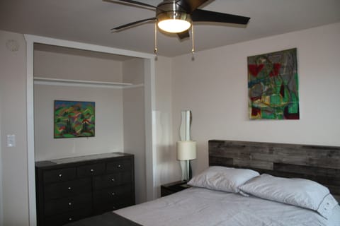 bedroom with queen bed and drawers and fan.