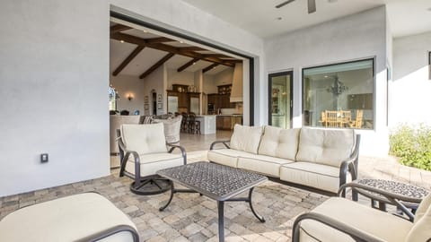 Covered patio lounge off living room through panoramic doors w/ backyard views.