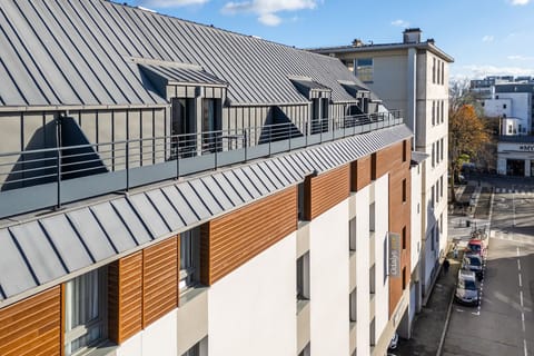The exterior showcases a contemporary design with a striking combination of sleek metal roofing and warm wooden panels, inviting guests into a modern space right in the heart of Rennes.