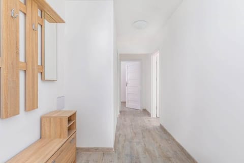 A bright hallway with a combination of white walls, wooden floors, and a wide passage leading into another room.
