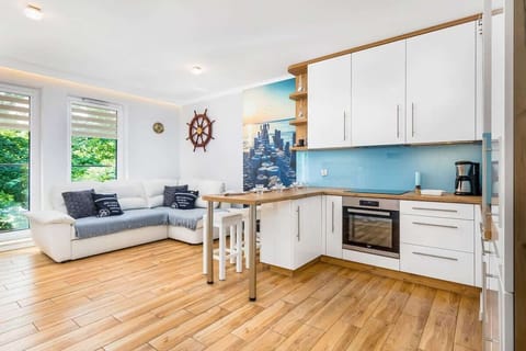 A spacious living room with a dining table and an open kitchen, featuring white cabinets and wooden flooring.