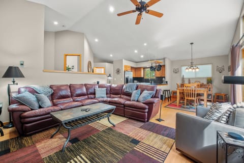 Bright and inviting living space featuring a large leather sectional, vaulted ceiling with ceiling fan, and seamless flow into the kitchen and dining areas. Perfect for entertaining or relaxing after mountain adventures.