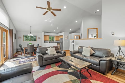 Bright open-concept living space featuring plush leather seating, vaulted ceilings with ceiling fan, and a seamless flow into the dining and kitchen areas for effortless entertaining.