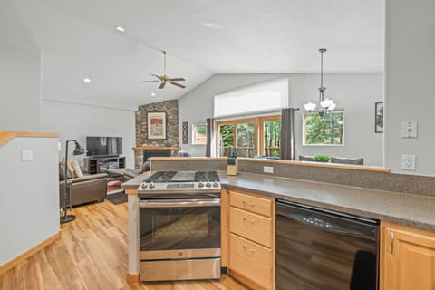 Contemporary kitchen with a sleek gas range and bar seating opens directly to a spacious living and dining area. Expansive windows and sliding doors bring in natural light and forest views, creating an inviting space for cooking and entertaining in the hea