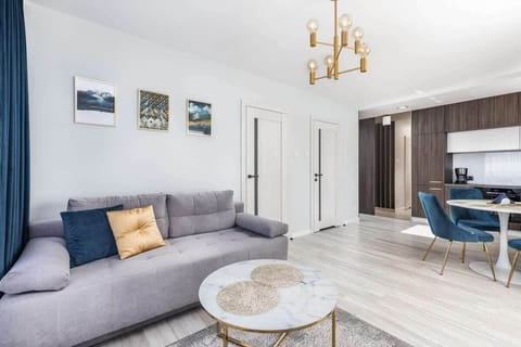 Living room with a gray sofa and a round coffee table. The decor features subtle, modern touches and a chandelier.