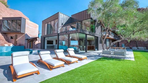 Striking modern home with a pool, lush lawn, and dramatic cliffside views.