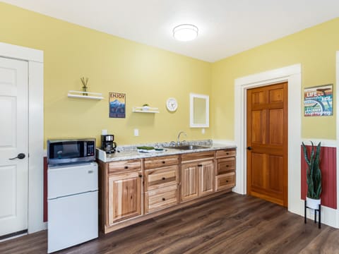 Ktichenette with microwave, coffee maker, mini-fridge, dishes, towel, sponge, soap and paper towels and sink.