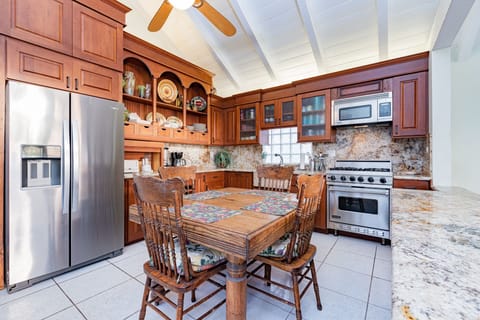 The kitchen overlooks the living area and beach beyond and includes a dining table with seating and additional bar stools at the kitchen counter.