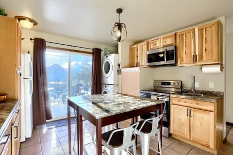 - Well equipped kitchen with stainless appliances, microwave, and electric stove
- Rustic wood cabinets, tile floors, and antler chandelier set the scene
- In unit washer and dryer tucked beside the fridge for long stay convenience