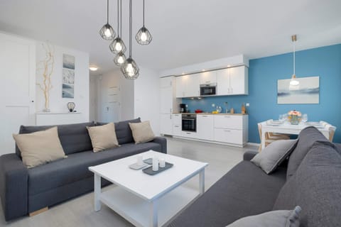 A cohesive combination of cosy living room and kitchen with a distinctive blue wall on which hangs a painting.