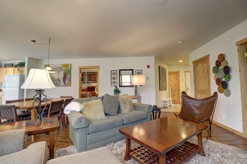 A cozy living room with a green sofa, wooden coffee table, tan butterfly chair, and modern decor. The room features a mix of contemporary and rustic elements, with art on the walls and a shag rug.