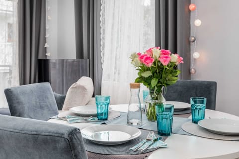 A close-up of a white table with a round top and tableware. A vase of flowers sits on the table.