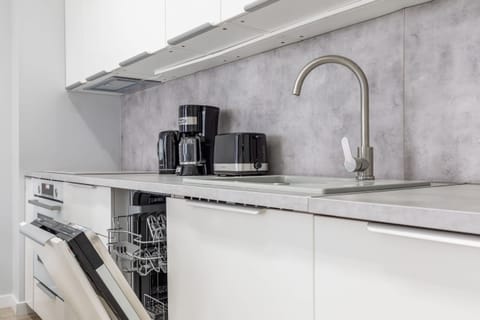 Close-up of the kitchenette with white cabinets and matching grey worktop. There is a dishwasher in the kitchen and a coffee machine and toaster on the countertop.