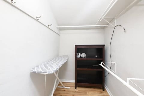 Spacious walk-in closet with multiple shelves for storage - Convenient ironing board included for guest use - Organized layout with hooks and hanging racks for clothes