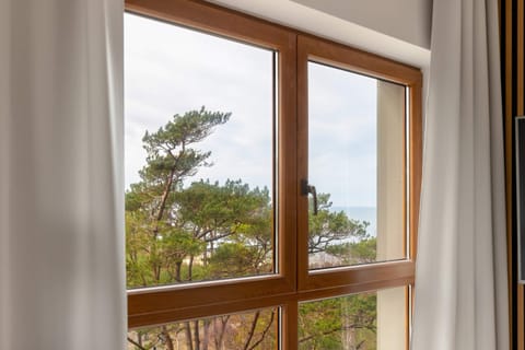A window view showing lush green trees from a cozy interior, with soft curtains framing the scene and natural light flooding the room.