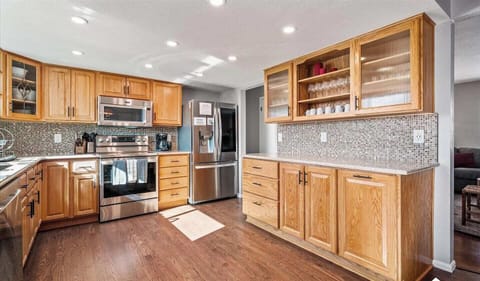 - Open kitchen layout with stainless appliances, sleek backsplash, and extra cabinetry
- Glass front upper cabinets make it easy to spot glassware and serving essentials
- Hardwood floors and soft lighting create a warm and functional cooking space