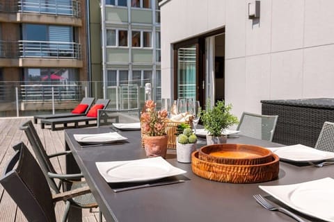Dine al fresco at this stylish outdoor table, set with elegant tableware, plants, and decorative details. Perfect for a relaxing meal or gathering with friends, surrounded by a cozy, sunlit atmosphere and modern seating.