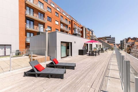 Relax on this spacious balcony with comfortable lounge chairs featuring vibrant red cushions. The area includes a dining table for outdoor meals, surrounded by modern glass railings, offering a perfect spot to unwind and enjoy the fresh air.