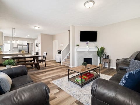 Step into this open-concept living area with cozy leather sofas, a stylish coffee table, and a modern fireplace topped by a wall-mounted TV. The space flows seamlessly into a dining area and bright kitchen for effortless entertaining! 🛋️🔥🍽️