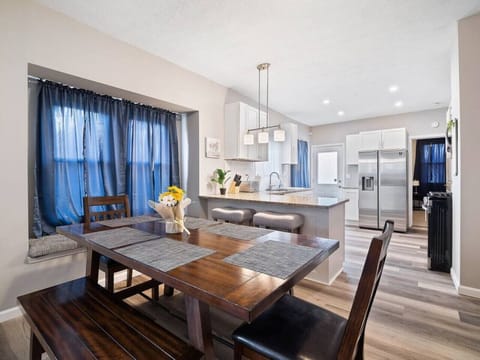 Cozy open space with leather sofas, wooden coffee table, and adjacent dining bench and chairs by bay window. Vinyl plank floors and blue curtains add warmth and style—perfect for relaxing and entertaining! 🛋️🍽️🏠