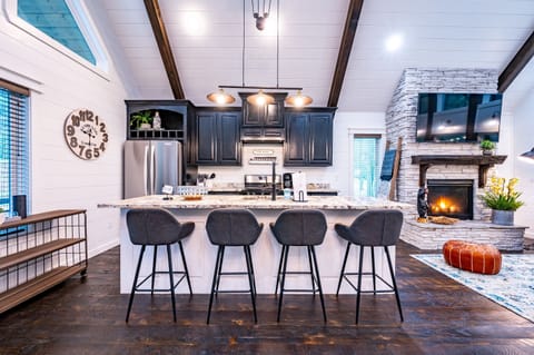 Fully stocked kitchen with ice machine, a dining table for six, and an open living room with a fireplace and TV above the mantle provide comfort and style.