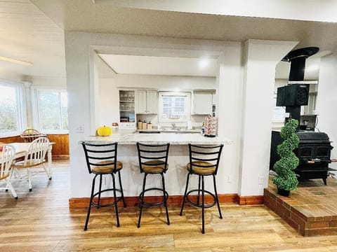 Cozy breakfast bar with seating for three, overlooking a well-equipped kitchen. Nearby, a wood-burning stove adds charm and warmth. Adjacent sunroom and dining area create a perfect flow for meals and gatherings during your vacation stay.






