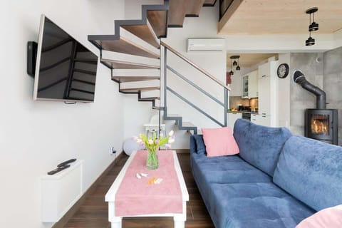 A living room area with a staircase, a blue couch, and modern decor with flowers on a table.

