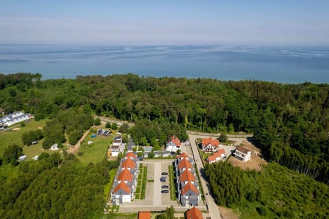 A bird's-eye view showing houses nestled near a lush green forest and open landscape.