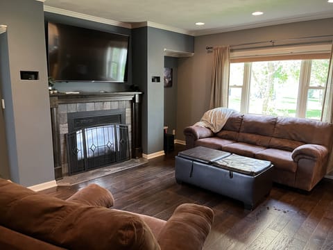 Living room with fireplace, TV, large bay windows to see a sliver of the lake