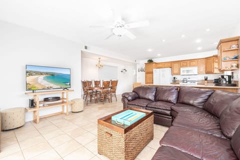 Sliding doors from the front patio open into the main living area, with large leather sectional, streaming TV, and kitchen and dining beyond.