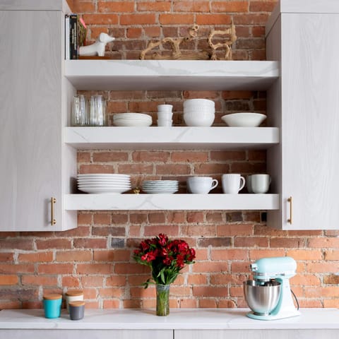 The “coffee bar” along the exposed brick wall, with shelves “that still show off the original brick” for plates, bowls, mugs, and glasses.