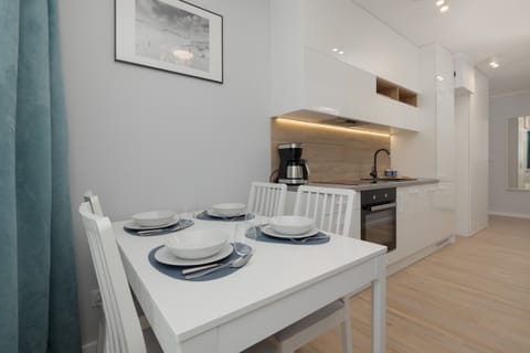 A modern dining area with a wooden table, white chairs, and an open kitchen in the background. The space is stylish and functional.