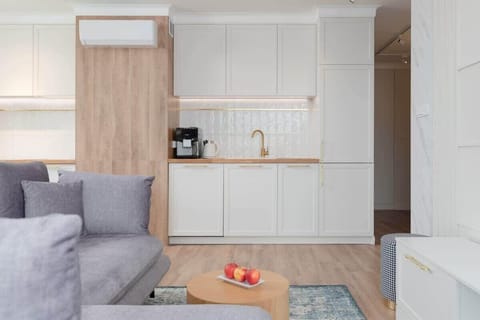 A compact yet functional kitchen with white cabinetry and gold fixtures. The design incorporates light wood accents for a modern and warm touch.