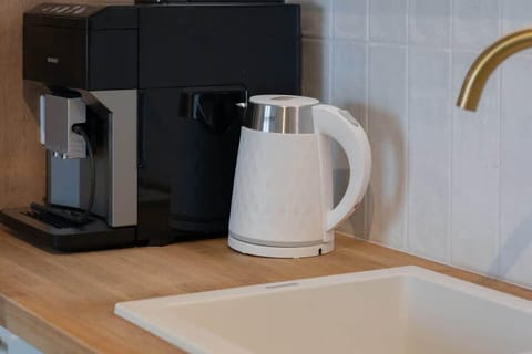A close-up of a coffee machine and kettle on a light wood counter, reflecting the kitchen's clean, functional design.