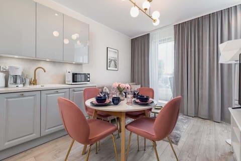 A dining area adjacent to a minimalist kitchen, with a round table and pink chairs.