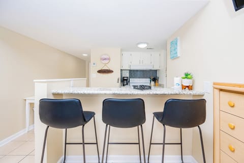 This kitchen features sleek granite countertops, a cozy bar area with black stools, and a charming coastal decor