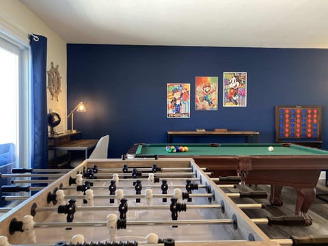 "The Game Room" featuring foosball, pool, wall-mounted connect 4, checkers, chess, dominoes, tic-tac-toe, a bar table with 3 stools, wall-mounted TV and slider leading to private balcony.