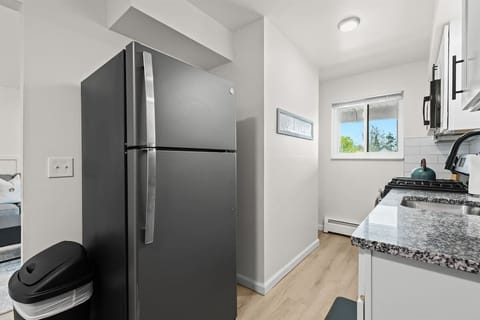 A sleek, modern galley kitchen features stainless steel appliances, white cabinetry, and granite countertops, with natural light streaming in through a window above the sink.