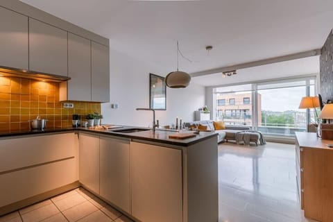 Bright open-plan living area flowing naturally to the terrace. Warm-toned kitchen featuring golden tiles and sleek modern design.
