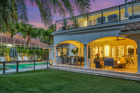 The covered patio contains a dining table for eight and a sitting area with TV and a fire pit. The backyard turf holds an outdoor kitchen equipped with bar seating for six and a grill.