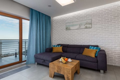 A cozy living room with a gray couch and blue curtains, featuring a wooden coffee table and a view of a balcony, letting in plenty of natural light.