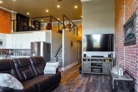 Living room area with smart TV and comfortable leather seating with open floor plan to the kitchen and dining areas.