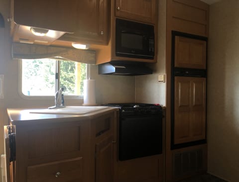 Inside RV, kitchenette with fridge, freezer, microwave, gas stove and sink. 