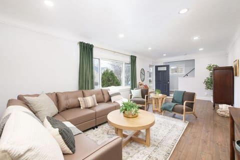 Bright living room with sectional sofa and modern seating   - Large windows with natural light and green curtains   - Stylish setup perfect for relaxing and gathering