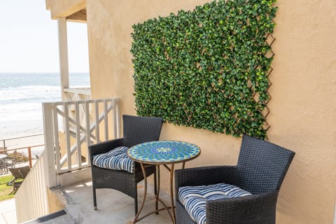 Ocean-view balcony with wicker chairs and mosaic bistro table at