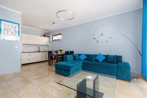 A bright, modern living room with a turquoise sofa, decorative pillows, and a flat-screen TV mounted on the wall.